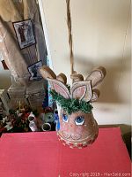 Photo of hanging reindeer bell decoration showing painted face, antlers, green tinsel on forehead and hanging rope.