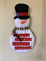 Front view of the full snowman advent calendar, showing the black top hat, colorful scarf, and all numbered pockets 1 to 24.