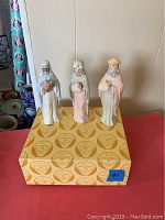 Three porcelain Three Kings figurines displayed on original yellow box with The Christopher Collection pattern on top. Figures include white, blue, pink and green in robes.