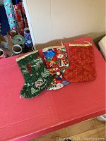 Three small quilted Christmas stockings displayed on a table with wrapping paper rolls in the background.