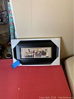 Snowman wall hanging in box placed on red surface against a wall.