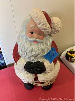 Front view of ceramic Santa figurine showing red suit, white beard, black gloves, and illuminated body.