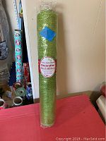 Roll of green decorative mesh ribbon standing vertically wrapped in clear plastic with label.