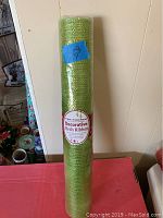 Photo showing the full roll of green decorative mesh ribbon standing upright with a price tag on it.