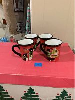 Four large ceramic mugs placed on a table, each with red background and penguin holding presents design.