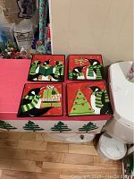 Photo of four square penguin-themed side plates with holiday designs on a red background, showing full plate set and details