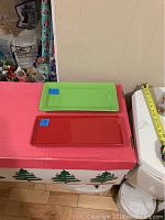 Two oblong serving plates on a table, one green and one red, with visible measuring tape showing lengths and widths.
