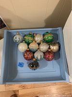 Set of 12 assorted spherical Christmas tree ornaments of various colors and glitter decorations in a blue container.