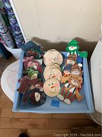 Blue tray filled with multiple wooden Christmas ornaments including different styles of snowmen and snowman faces.