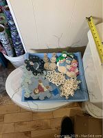 Top view of blue tray holding various wooden Christmas ornaments including snowmen, snowflakes, and Santa Claus figures with wires for hanging.