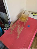 Full view of gold metal mesh sleigh with attached reindeer on red surface.