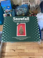 Photo of the green Snowfall box with white snowflakes and text detailing the product, including image of artificial Christmas tree with snow effect.