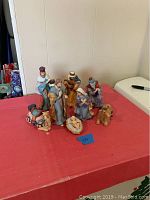 Full view of the eight-piece ceramic nativity set arranged on a red cloth, showing all figures including Mary, Joseph, Baby Jesus, Wise Men, shepherd, and camel.