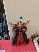 Full view of the standing angel figurine displaying its red and green clothing and gold wings.