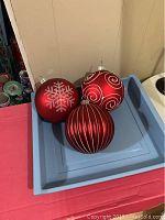 Three large red Christmas balls with silver decoration displayed on a blue plastic bin to highlight size and decorations.