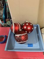 Three large red Christmas balls in a blue plastic container, showing different silver decorative patterns.