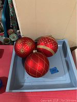 Three large red Christmas balls with gold glitter patterns in a light blue tray.