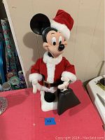Front view of Mickey Mouse Santa figurine wearing red and white Santa suit, holding black bag.