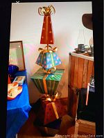 Full view of tall stacking metal present decoration resembling four layered gift boxes in various colors and patterns with gold ribbon detailing.