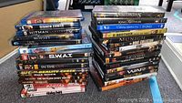 Photo of 31 DVD and Blu-ray cases stacked in two piles showing various movie titles including Man of Fire, Legion, Munich, Anacondas
