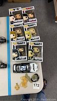 Six boxed Funko Pop vinyl figures featuring characters from movies and TV, an Alltel Ryan Newman model race car, pendant, necklace, bracelet and stones on table.