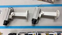 Two Philips digital color security cameras mounted on white wall brackets shown side by side. The cameras appear dusty from outdoor use.