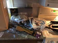 Photo of Emerald stainless steel fry pan box and several cooking utensils including wooden spatulas and wrapped items on countertop.