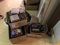 Photo showing multiple boxes filled with DVDs, CDs, and cassettes packed together on floor.