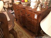 View of wooden sideboard from side angle showing structure, three drawer fronts, brass handles, and decorative details.