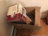 Box containing Rival Crock-Pot slow cooker in branded box, placed on floor.