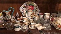 Various ceramic tea set pieces, glasses, bowls, and decorative items on dark wooden shelf