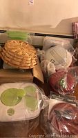 Photo showing woven basket, covered bowls, Apple cookie jar, and plastic food storage container with green lid.