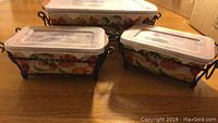 Three ceramic rectangular pans with plastic lids stacked in decorative black metal stand with fall leaf motif