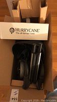 Box open showing HurryCane all-terrain cane components including folded cane parts inside box with packaging showing brand name.