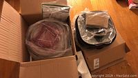 NuWave oven components packed inside an open cardboard box, wrapped in plastic and bubble wrap.