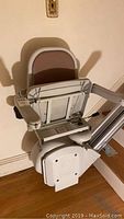 Side view of Acorn chairlift showing padded seat with folding backrest and footrest, mounted on stairway adjacent wall.
