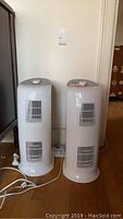 Front view of two upright white Hunter air purifiers side by side on hardwood floor with power cords
