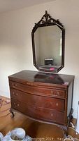 View of the dresser with bowed front, decorative drawer pulls, and octagon mirror mounted above it, showing some surface wear and scratches.