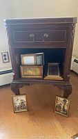 Full view of vintage wooden side table showing single drawer, claw feet, surface wear and included picture frames inside the open shelf