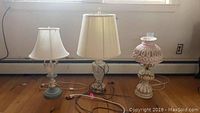 Three lamps and small powerstrip lined up on floor under window showing various lamp styles and cords.