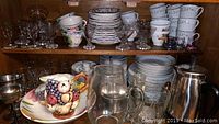 Wooden shelf filled with multiple shelves of dinnerware including plates, bowls, cups, glassware, and ceramic pitcher.