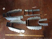 Top view of several metal joist hangers arranged on wooden surface next to a ruler for size reference. Some are wide plate hangers (5.5 inch), others narrower heavy duty 3.5 inch wide.