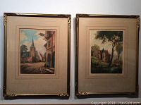 Overview of the two framed English engraving block prints displayed side by side on a wall showing matching frames with antique village scenes.