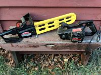 Sears Craftsman 3 inch belt sander and Mastercraft 10AMP electric chainsaw side by side on wooden bench outdoors.