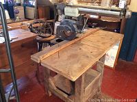 Wide view of the radial arm saw mounted on a large wooden table base with a solid work surface and storage underneath.