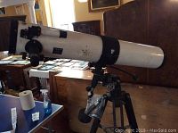 Side view of white Tasco telescope mounted on wooden tripod with extra lenses hanging.