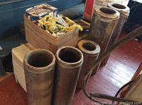 Five metal stove pipe sections arranged on floor and chair, with signs of rust and wear. One shorter section around 6 inches and four longer sections about 7 inches each.