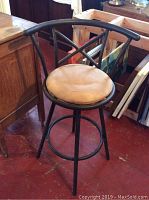 Side angle showing black metal stool frame, cushioned round seat, swivel mechanism, curved backrest and footrest ring.