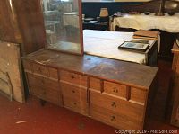 Front and top view of the wooden dresser showing nine drawers with varying metal pulls, surface scratches, and attached mirror.