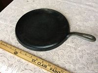 Top view of cast iron griddle with a 12 inch ruler for scale, showing smooth round cooking surface and handle
